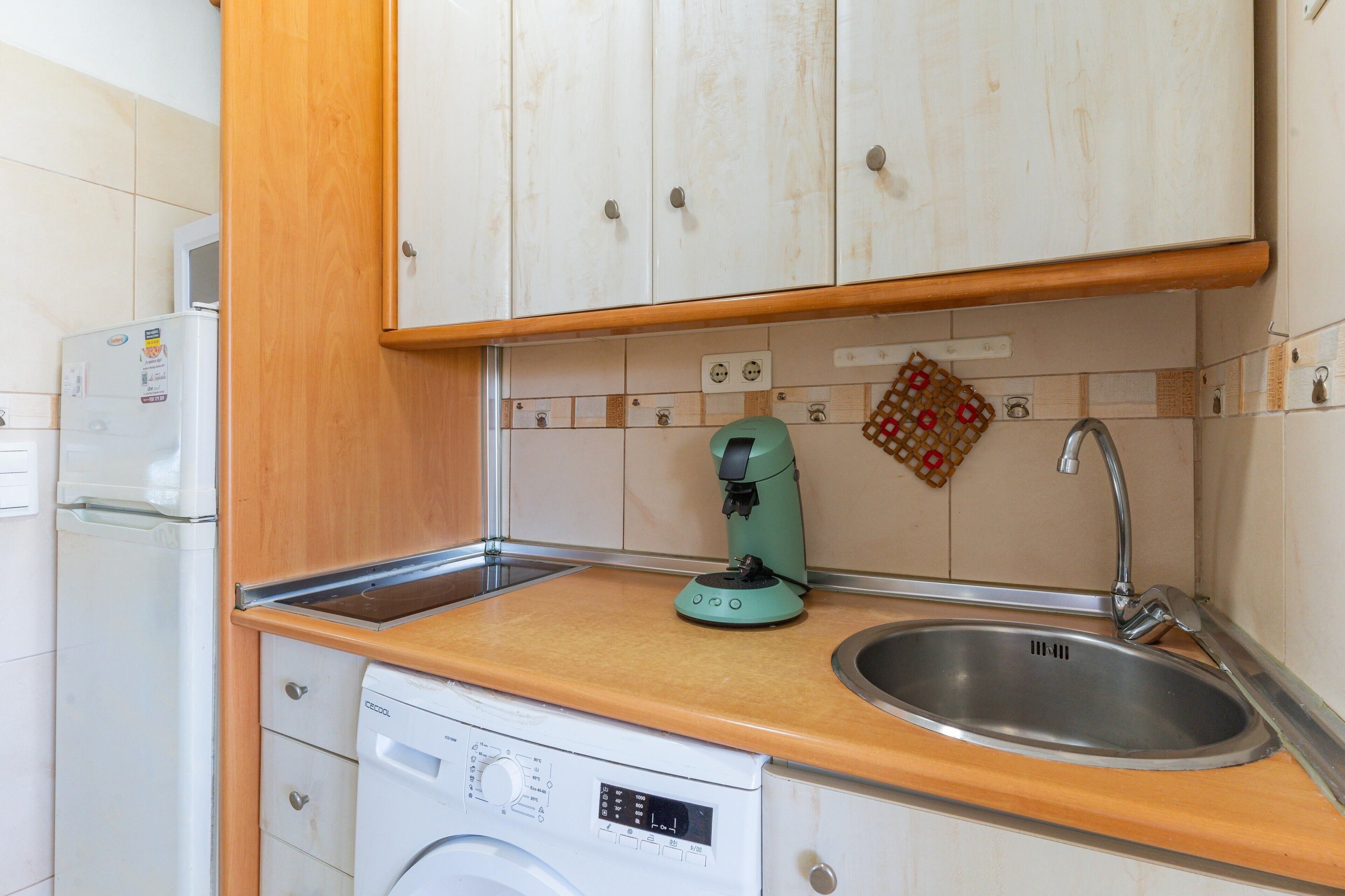 Una cocina compacta con lavadora, cafetera y pileta.