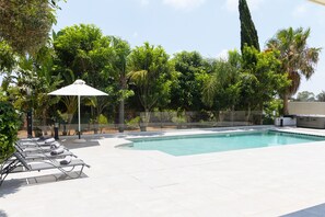 Ein Swimmingpool mit Liegestühlen und Sonnenschirm, umgeben von üppiger Vegetation.