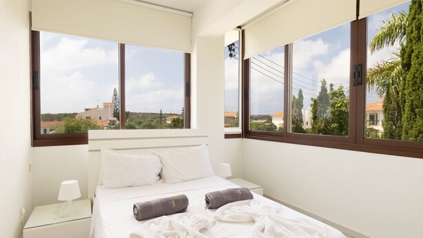 Una camera d'albergo con un letto, due cuscini, un comodino, una lampada e ampie finestre con vista sui dintorni.