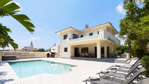 Una casa a due piani con piscina, area salotto esterna e antenna parabolica.