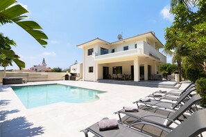 Ein zweistöckiges Haus mit Swimmingpool, Sitzgelegenheiten im Freien und einer Satellitenschüssel.