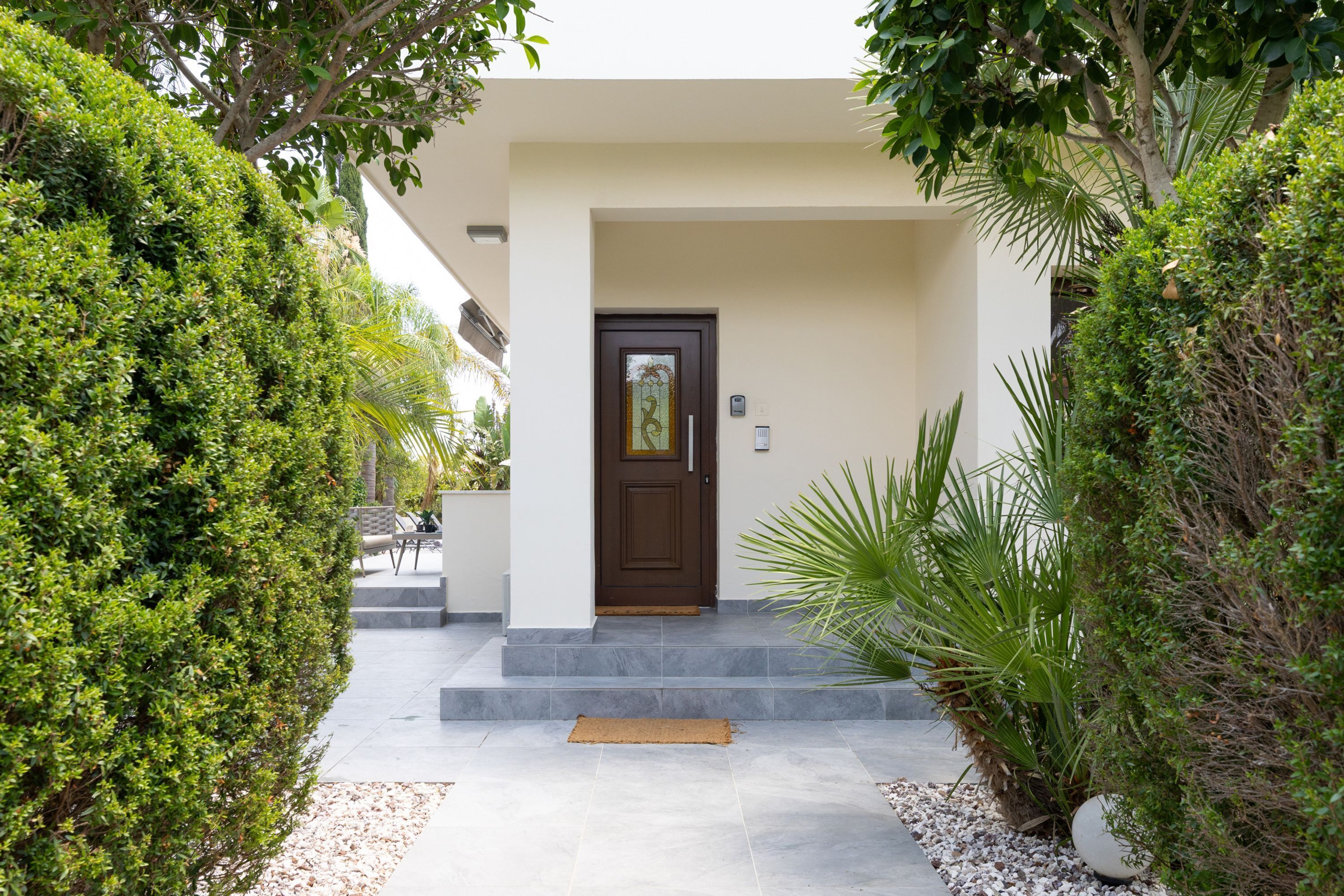 A modern entrance with a brown door, a small porch, and a pathway leading to the door.
