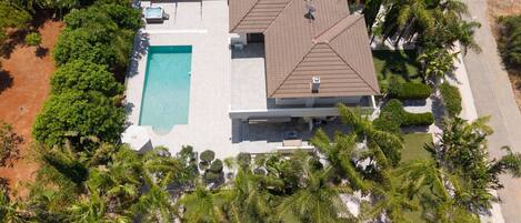An aerial view of a modern house with a swimming pool, satellite dish, and lush landscaping.