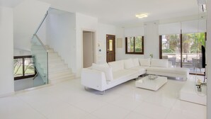Un soggiorno moderno con un divano angolare bianco, una scala in vetro e un'area da pranzo con vista sull'esterno.