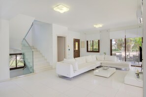 Ein modernes Wohnzimmer mit einem weißen Modulsystem, einer Glaskonstruktion als Treppe und einem Essbereich mit Blick ins Freie.