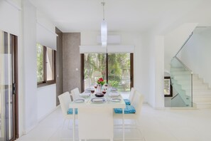 Un espace de salle à manger moderne avec une table dressée pour six personnes, un escalier et de grandes fenêtres.