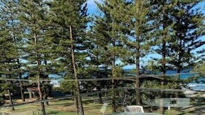 A glass-top table with white chairs on a patio with a view of trees and a body of water. - Lovely Beachfront Three Bedroom Unit (Gold Coast)