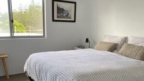 A bedroom with a bed, a nightstand, a lamp, a framed picture on the wall, and a window. - Lovely Beachfront Three Bedroom Unit (Gold Coast)
