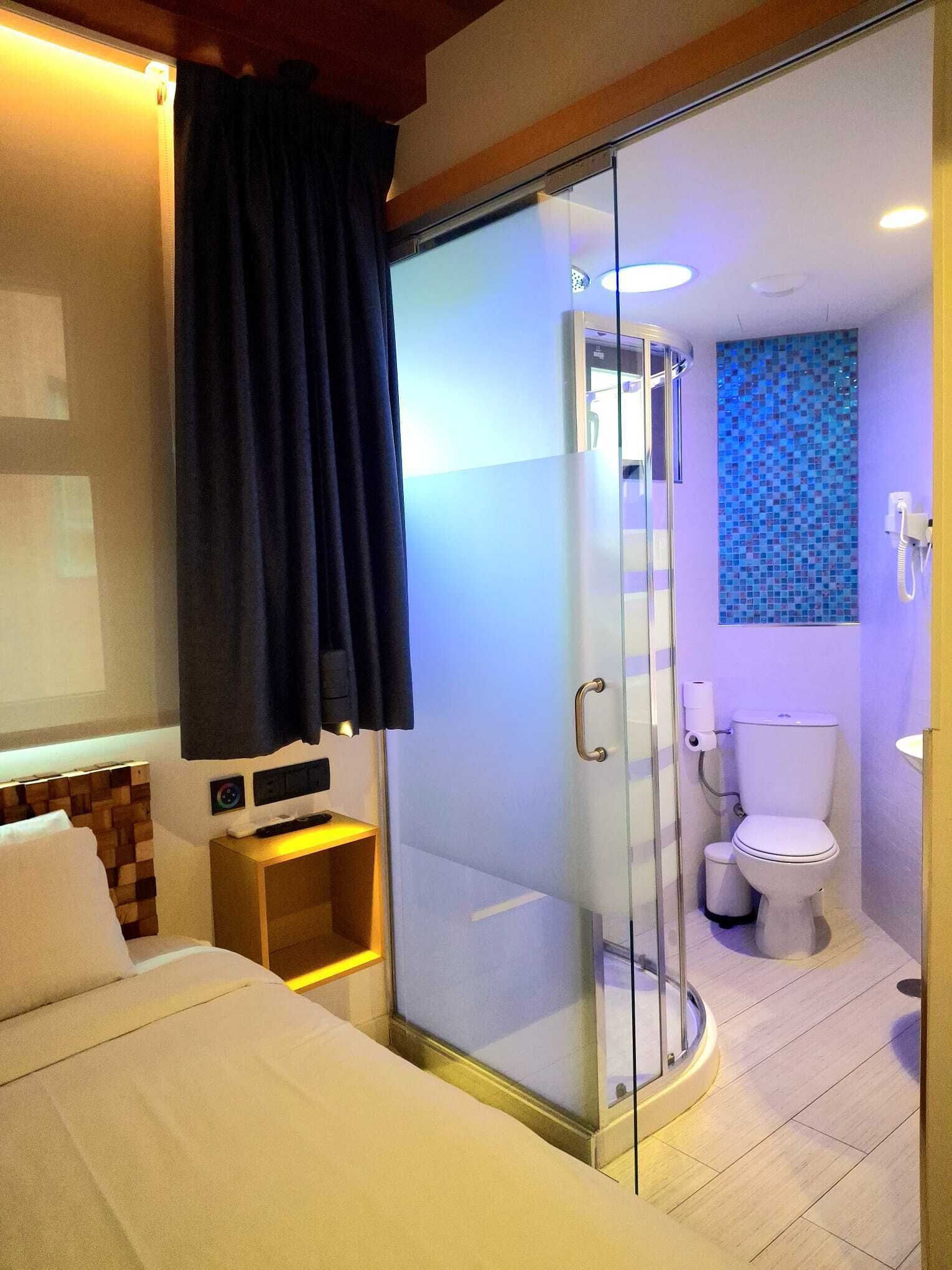 Hotellihuone, jossa on sänky, yöpöytä, lasiseinällä varustettu suihku, wc ja seinään kiinnitetty puhelin.