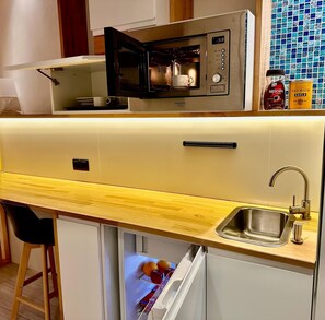 Kompakti keittiö, jossa on sisäänrakennettu mikroaaltouuni, pesuallas ja jääkaappi.