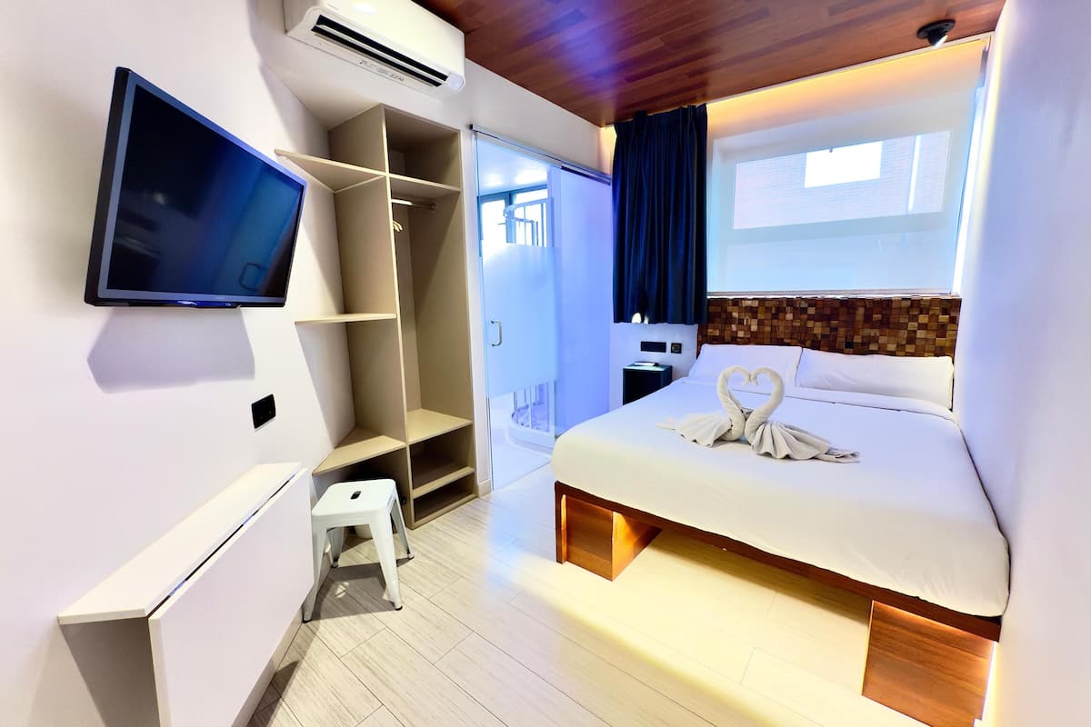 Quarto de hotel moderno com cama, televisão, guarda-roupa e um pequeno banquinho.