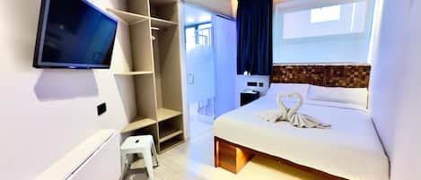 A modern hotel room with a bed, a TV, a wardrobe, and a small stool.