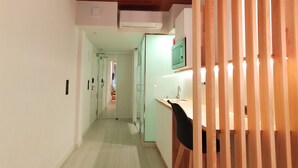 Un pasillo estrecho con un separador de madera a la derecha, una zona de cocina con un lavamanos y armarios, y una puerta que da a otra habitación.