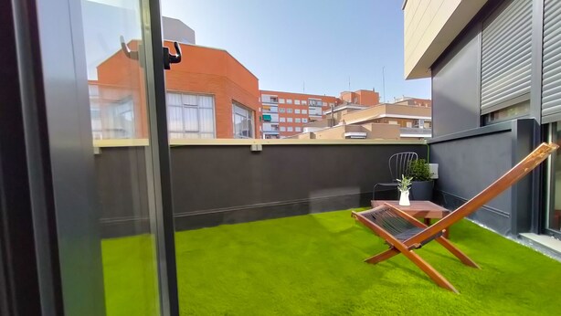 A balcony with artificial grass, a wooden chair, and a small table with a potted plant. - Far Home Suites (Madrid)