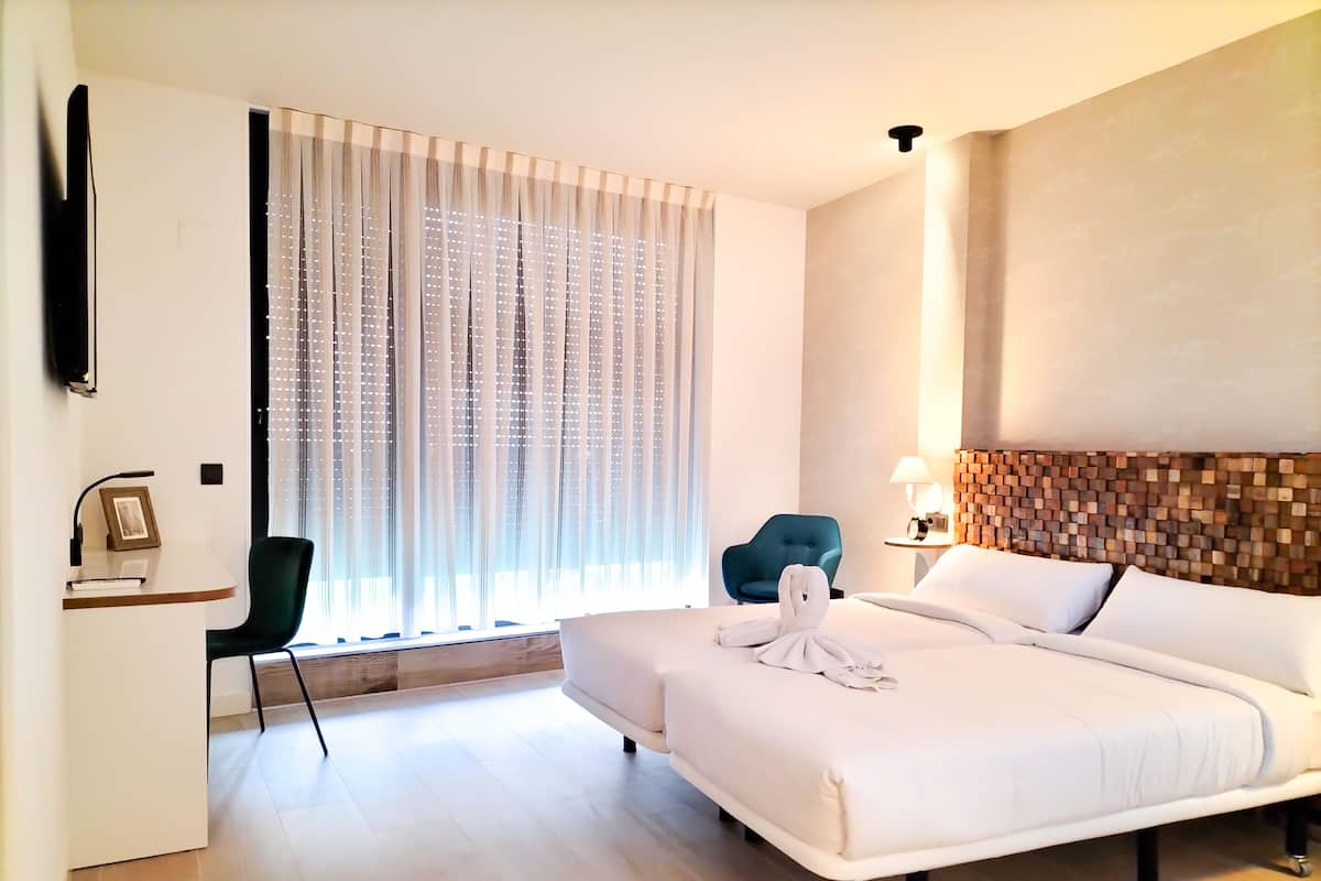 Quarto de hotel com cama, escrivaninha, cadeira, televisão e janela com cortinas.
