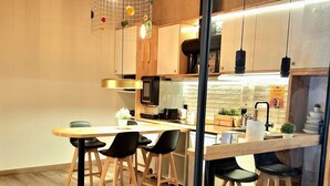 A modern kitchen with wooden flooring, a central island, bar stools, and pendant lighting. - Far Home Suites (Madrid)