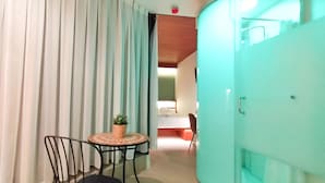 A room with a bed, a small table with a plant, and a chair. There is a curtain and a door with a handle. - Far Home Suites (Madrid)