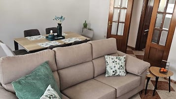 A living room with a beige sofa, a dining table, and a small side table.