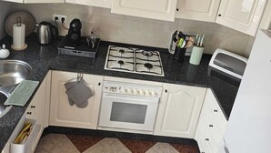 Una cocina con gabinetes blancos, estufa a gas, microondas y refrigerador.