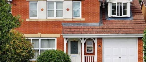 A two-story brick house with a front porch, a garage, and a well-maintained lawn.