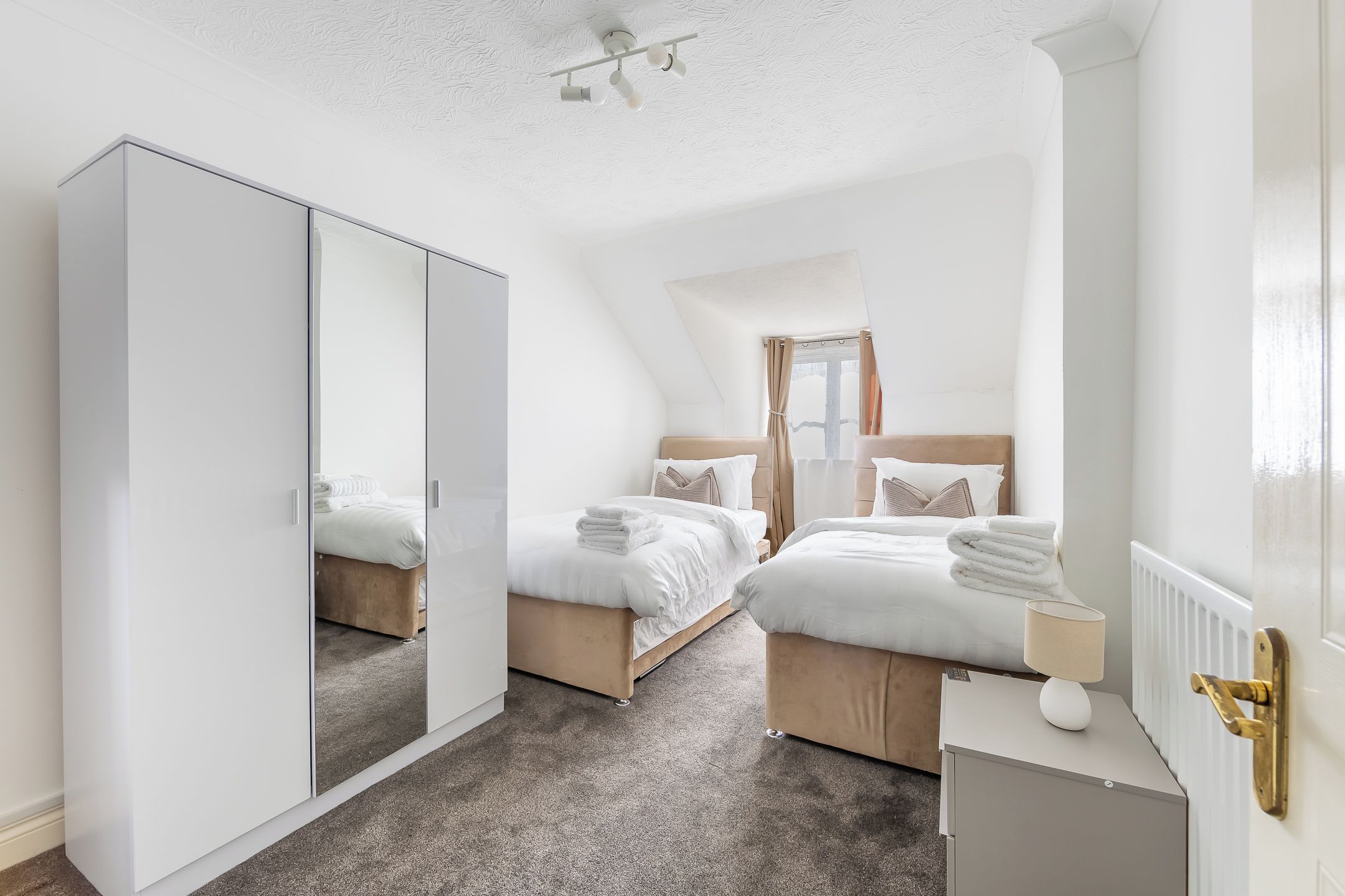 A bedroom with two beds, a wardrobe, a radiator, and a ceiling fan.