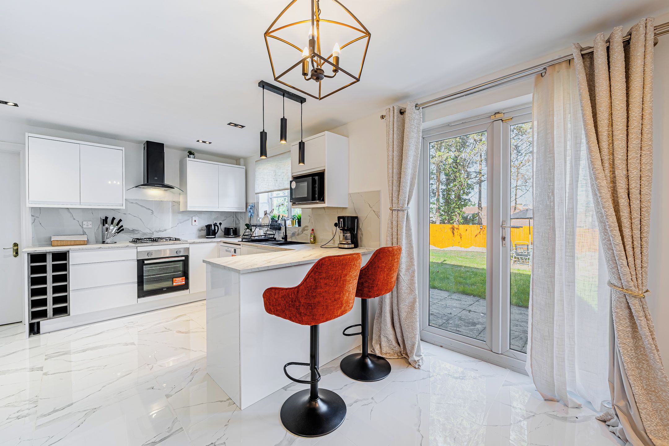A modern kitchen with white cabinets, a central island, and a dining area with two red chairs.