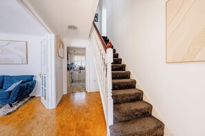 A staircase with a wooden handrail and carpeted steps leading to a kitchen area. - Luxury 4 Bedroom Home, Sleeps 10, Garden, Free Parking, Hornchurch, Near London (Hornchurch)