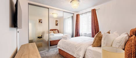 A hotel room with a bed, a flat-screen TV, a wooden side table, a lamp, and a mirror.