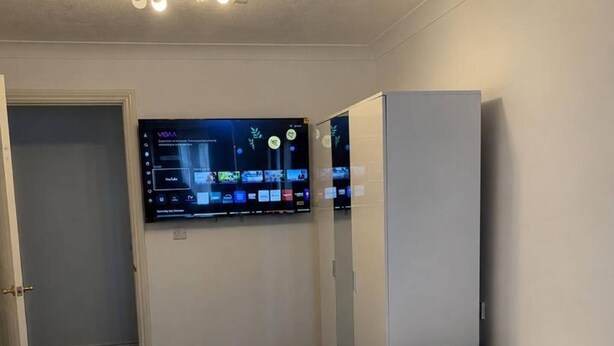 A bedroom with two beds, a TV mounted on the wall, and a door.