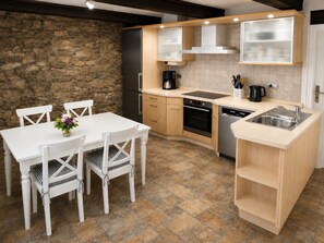 A compact kitchen with a stone wall, a dining table with chairs, and modern appliances. - Spacious two-bedroom vacation rental in the historic district of Wernigerode. (Wernigerode)