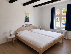 A double bed with a wooden frame and white bedding, two bedside tables with lamps, a framed picture on the wall, and a window with curtains. - Spacious two-bedroom vacation rental in the historic district of Wernigerode. (Wernigerode)
