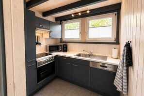 A compact kitchen with a stove, microwave, sink, and cabinets. - Skandinavisches Ferienhaus mit Privatsauna im Hafendorf Müritz (Granzow)
