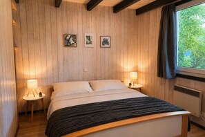 Ein Schlafzimmer mit einem Bett, zwei Nachttischen mit Lampen, einem Fenster mit Vorhängen und drei gerahmten Bildern an der Wand.