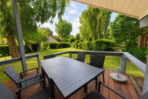 Een terras buiten met een tafel en stoelen, omringd door een houten terras en een witte balustrade.