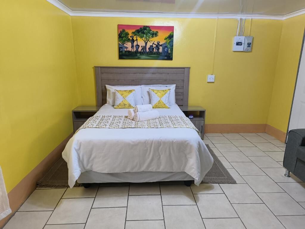 Una habitación con cama, mesitas de noche, un cuadro en la pared y un enchufe.