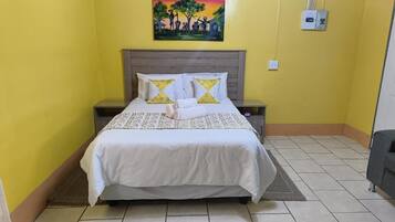 Una habitación con cama, mesitas de noche, un cuadro en la pared y un enchufe.