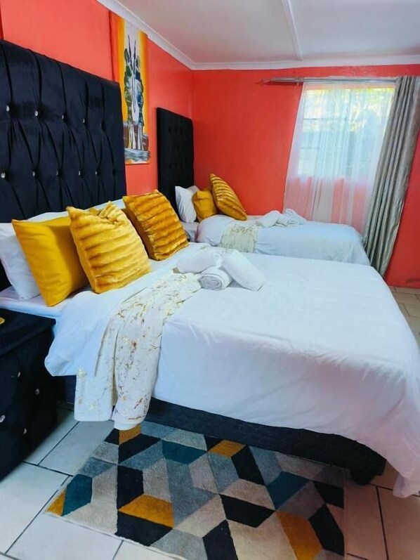 A double bed with white bedding and multiple pillows, a black headboard, and a patterned rug.