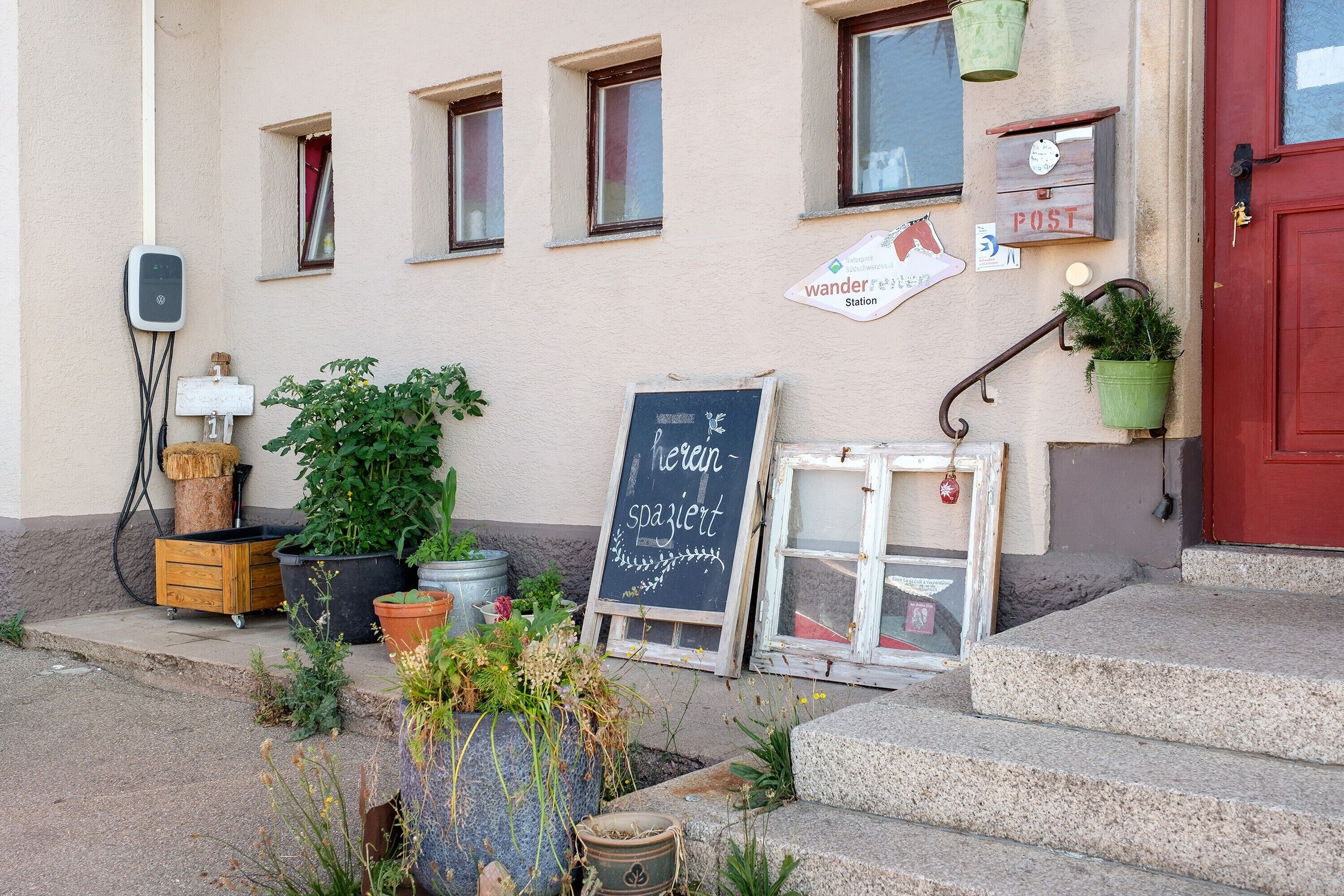 Ein Gebäude mit roter Tür, einer Kreidetafel und Topfpflanzen.
