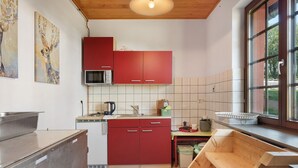 A kitchen with red cabinets, a microwave, a sink, and a window with a view of greenery. - Tiny Home “Bauwagen auf dem Falkenhof” – Nature Retreat with Shared Kitchen (Eisenbach)