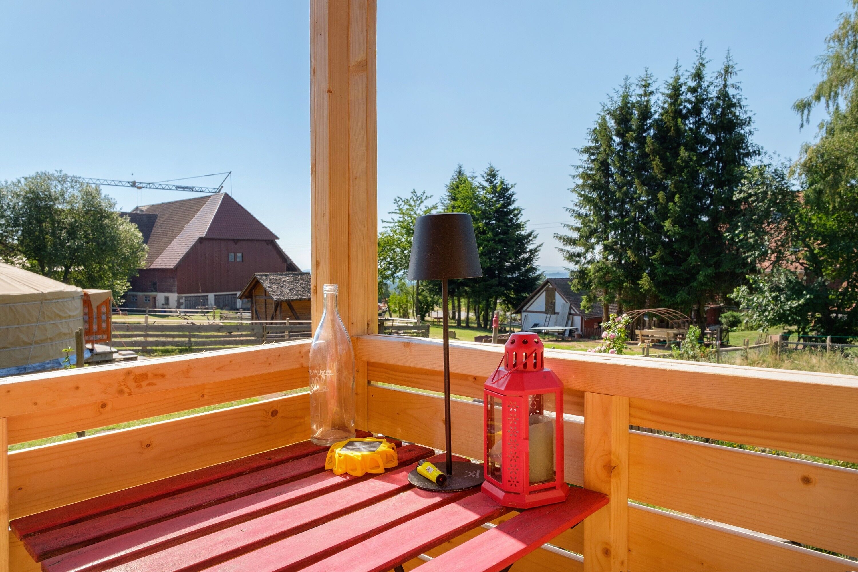 Eine Holzterrasse mit einer roten Bank, einem roten Laternenleuchter, einer klaren Glasflasche und einem gelben Gegenstand.