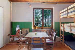 A room with a wooden table, chairs, a bunk bed, and a window with a view of trees.