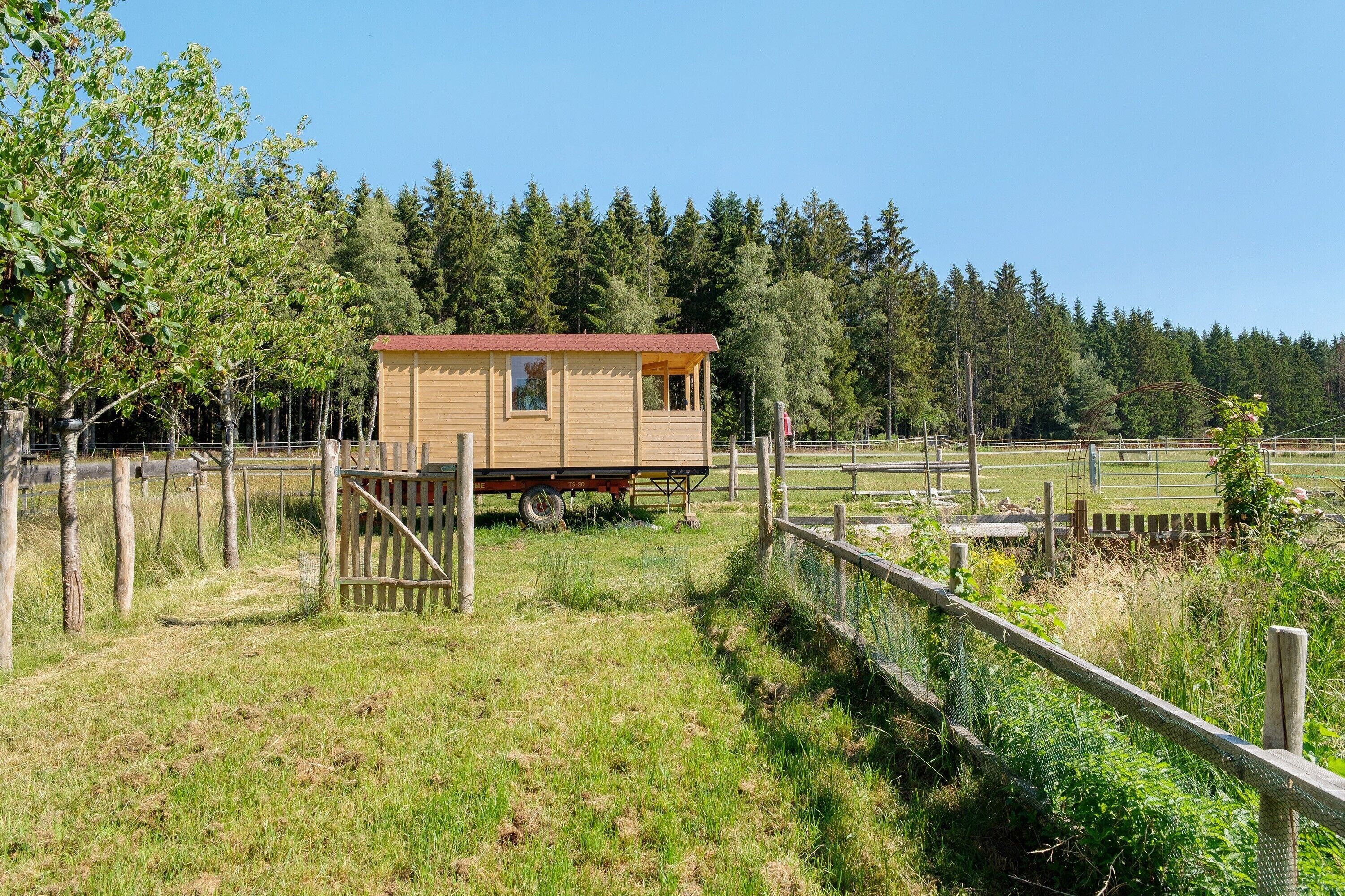 Une cabane en bois avec un toit rouge, entourée d’une clôture et d’arbres.