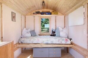 A cozy bedroom with a wooden ceiling, a bed with floral bedding, a small window, and a bedside table with a lamp.