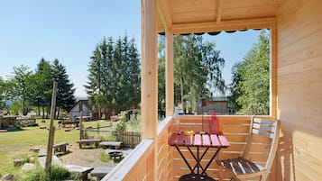 Een houten terras met een tafel en stoelen, uitkijkend op een gazon met bomen en een gebouw op de achtergrond.