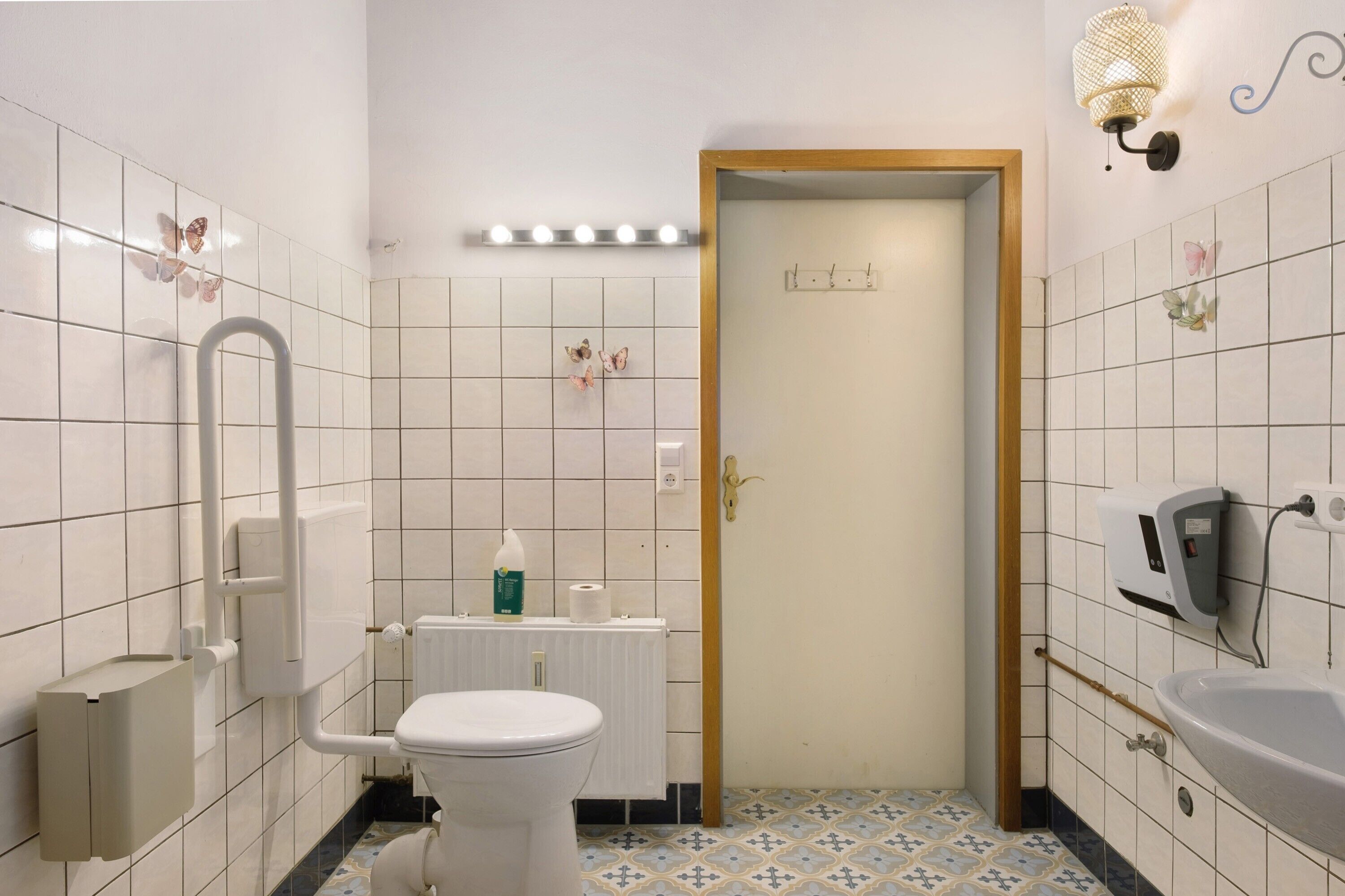 Ein Badezimmer mit Toilette, einem Handtrockner, einem Papierhandtuchspender und einem Seifenspender.