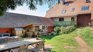 Un espace extérieur rustique avec une table et des chaises en bois, un coin salon abrité et un jardin clôturé.