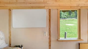 A bedroom with a wooden ceiling, a bed with a floral bedspread, a window with a view of a grassy area, and a whiteboard on the wall.