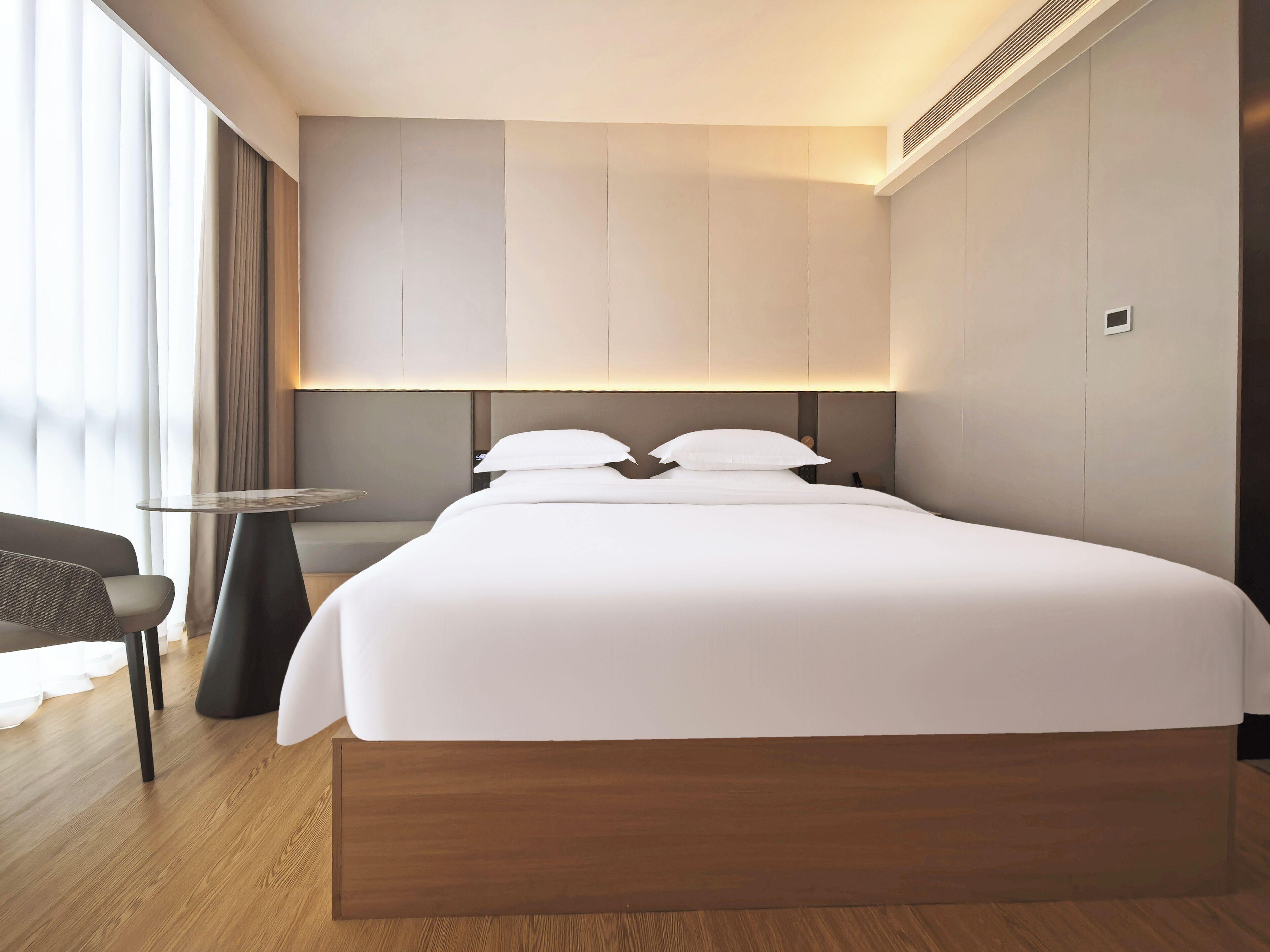A modern hotel room with a large bed, a small round table, and a chair.