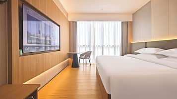 Une chambre d’hôtel avec un lit, un bureau, une chaise, un téléviseur fixé au mur et une fenêtre avec des rideaux.