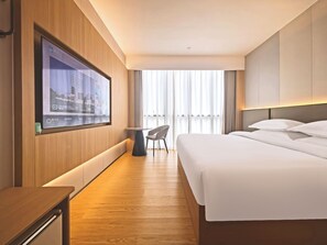 Hotelkamer met een bed, bureau, stoel, tv aan de muur en raam met gordijnen.